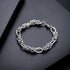 A silver rope-link bracelet displayed on a sleek black surface, showcasing its detailed interlocking rings and polished finish.