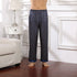 Model wearing dark blue silk pajama pants with circular geometric pattern and blue cuffed hem, standing barefoot on wooden floor by white nightstand