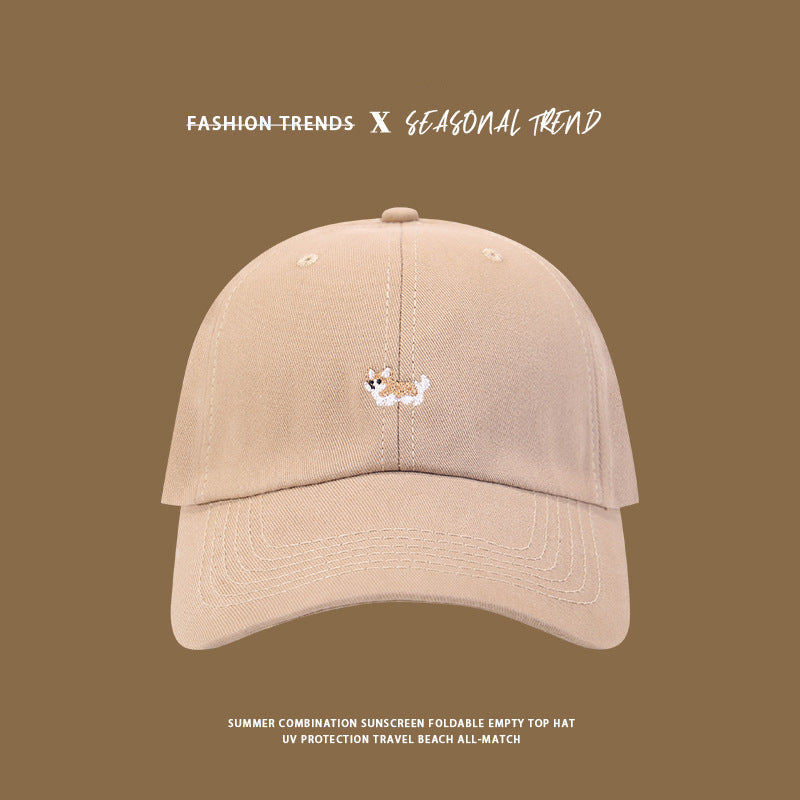 Beige baseball cap with small corgi embroidery shown against brown background