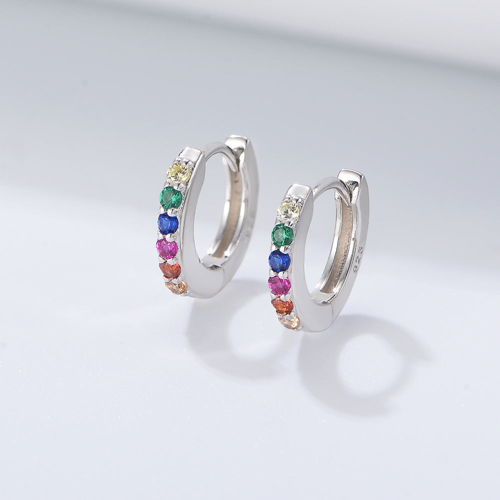 A pair of silver 925 huggie hoop earrings with rainbow colored gemstones displayed on gray background