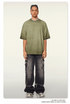 Model with braided hair wearing olive green oversized t-shirt with slight wash effect, silver chain necklace, distressed cargo jeans