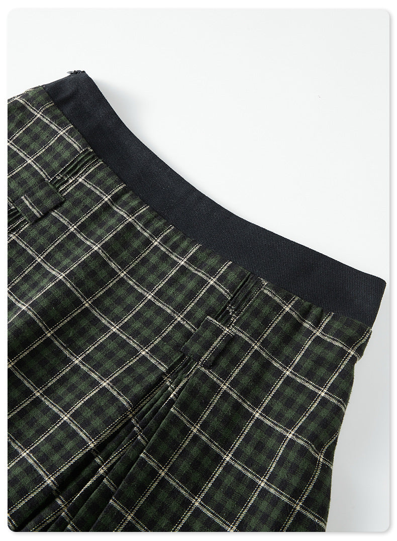 Close-up of green plaid skirt waistband with black elastic band against white background