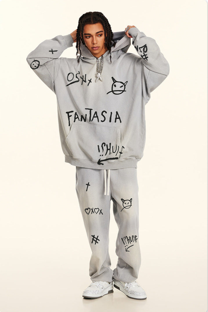 Full body shot of model in oversized gray sweatsuit with black spray-painted symbols and 'FANTASIA' text, paired with white sneakers