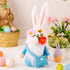 A blue-dressed bunny gnome with a felt crossbody bag, white beard, and floral hat, surrounded by pastel-colored Easter decorations.