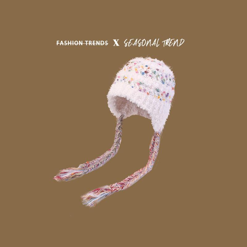 White fuzzy winter hat with multicolored speckles and braided earflaps, emphasizing cozy winter fashion