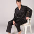 Male model seated in elegant white chair wearing black striped silk pajamas with open collar detail