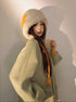 Cream furry winter hat with orange lightning bolt detail and pom-pom ties, modeled in profile
