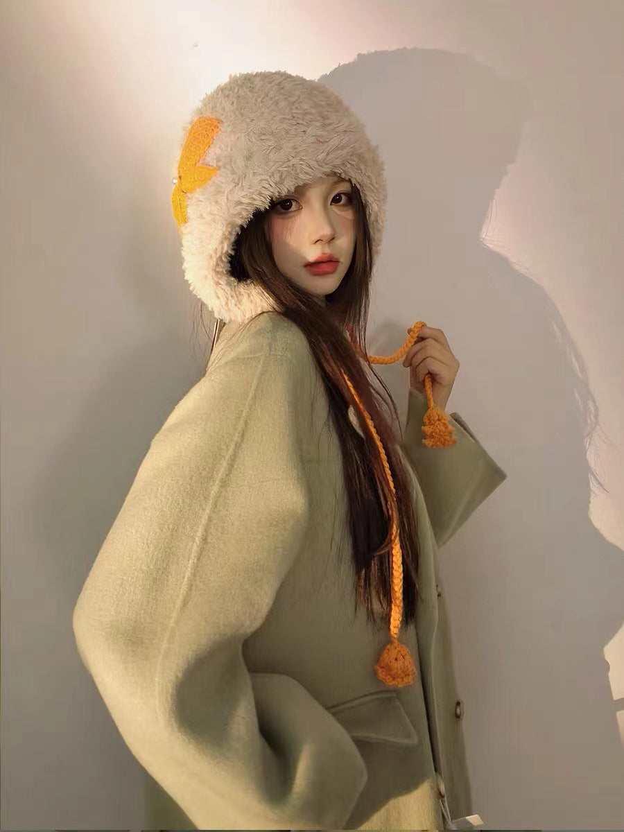 Cream furry winter hat with orange lightning bolt detail and pom-pom ties, modeled in profile