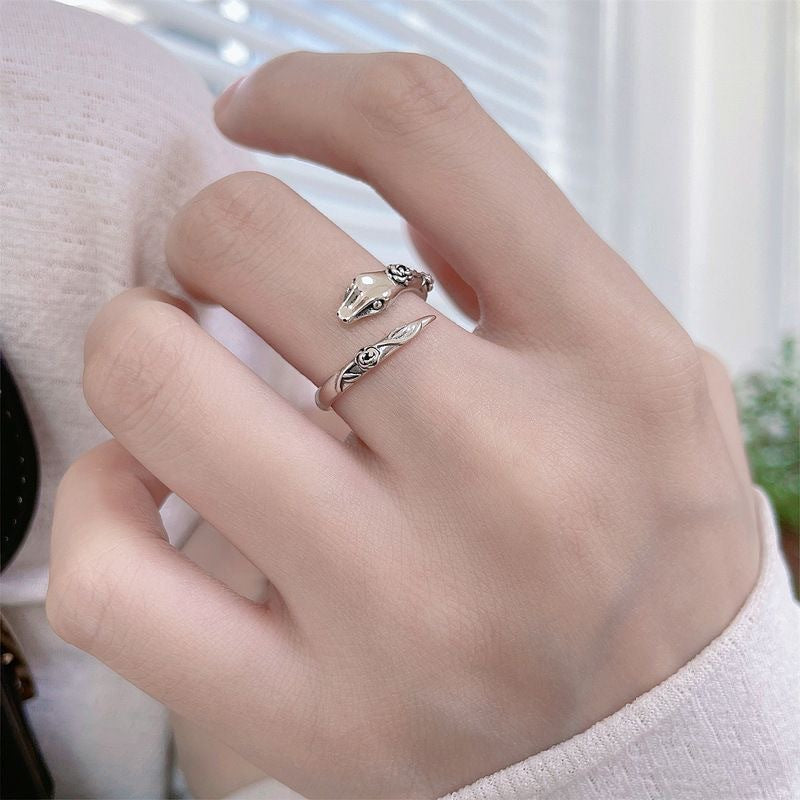 A model is wearing a silver adjustable snake ring with rose details on their finger. Soft natural lighting by window