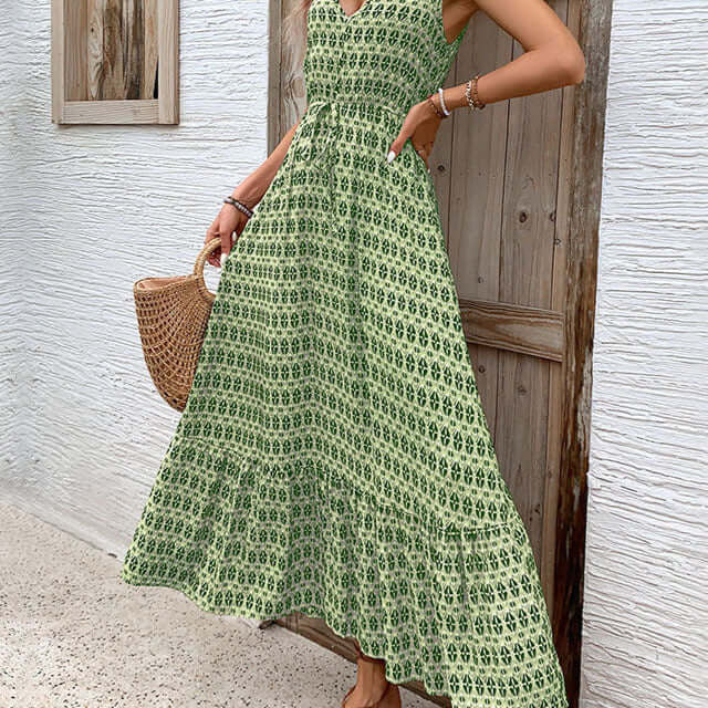  Woman in a green printed boho maxi dress, standing near a wooden door, accessorized with gold jewelry and strappy sandals.