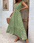  Woman in a green printed boho maxi dress, standing near a wooden door, accessorized with gold jewelry and strappy sandals.