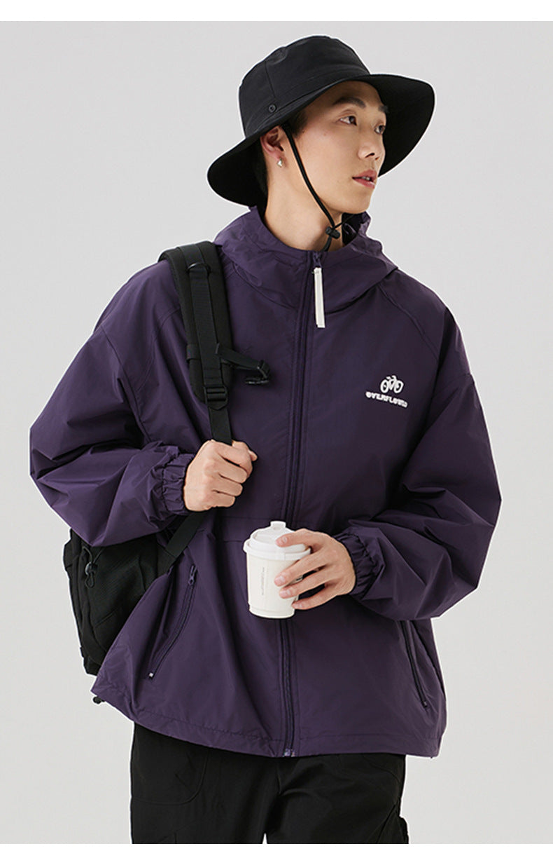 A man wearing purple windbreaker jacket with white zipper pull, black bucket hat and backpack, holding coffee cup against white background