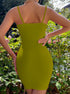 A woman wearing olive green ribbed mini dress with straight neckline stands with hand on hip against garden foliage