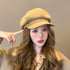 Woman in beige newsboy cap with wavy brown hair and coordinating beige outfit against neutral background