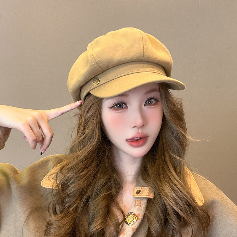 Woman in beige newsboy cap with wavy brown hair and coordinating beige outfit against neutral background