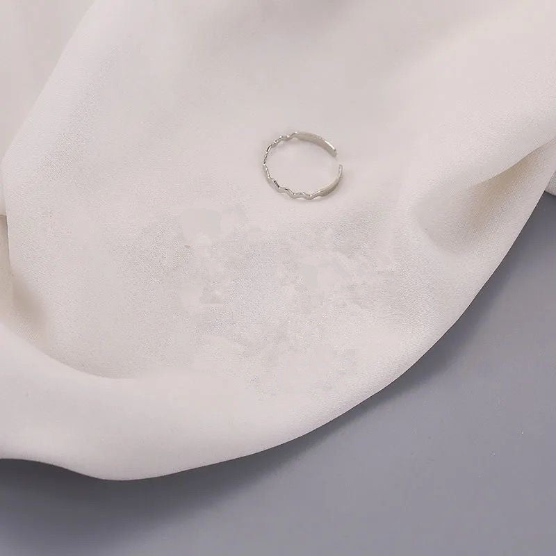 A delicate silver twisted band ring displayed on soft white fabric with minimal styling