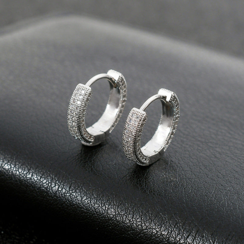 Pair of silver tone pave crystal huggie hoop earrings displayed on black leather surface, showing detailed small stone setting
