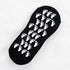 Close-up of black ankle sock with white footprint grip pattern on sole displayed flat against white fabric background