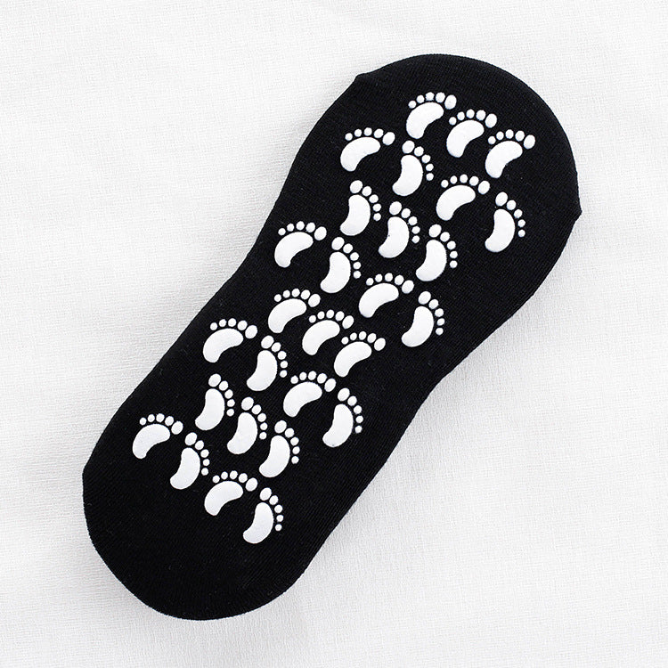 Close-up of black ankle sock with white footprint grip pattern on sole displayed flat against white fabric background