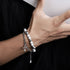 A person giving a thumbs-up while wearing a stylish silver and white beaded bracelet with a cross pendant, paired with a black outfit for a modern look.