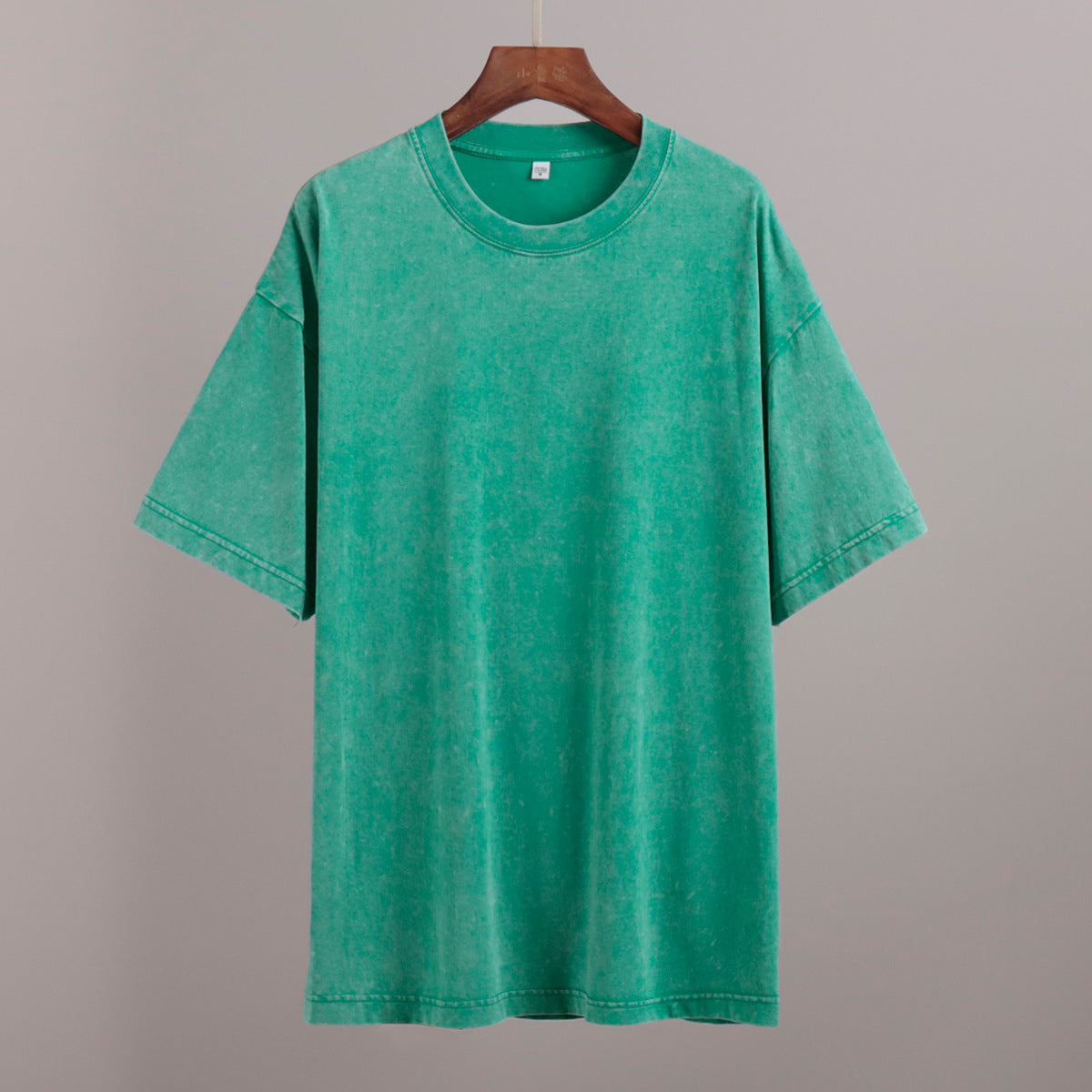 Green t-shirt on a wooden hanger against a gray background