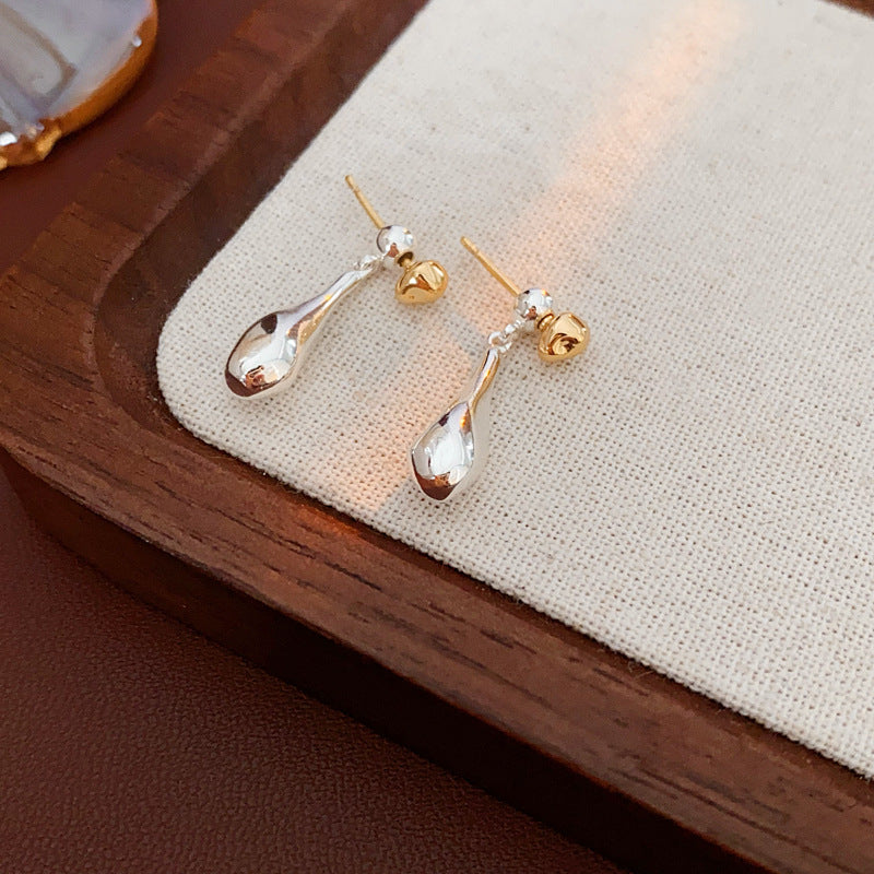 Silver teardrop earrings with gold ball studs on textured background