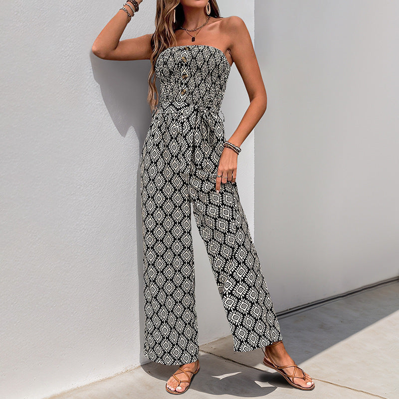 Woman walking outdoors in a strapless black and white jumpsuit with a cinched waist, paired with strappy sandals and gold jewelry.