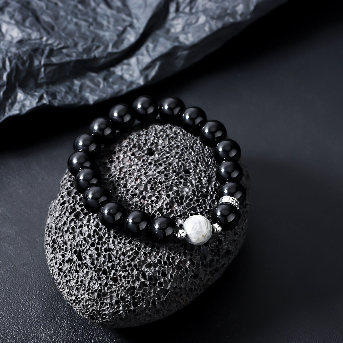 Black and gray beaded bracelet resting on a textured black stone surface.