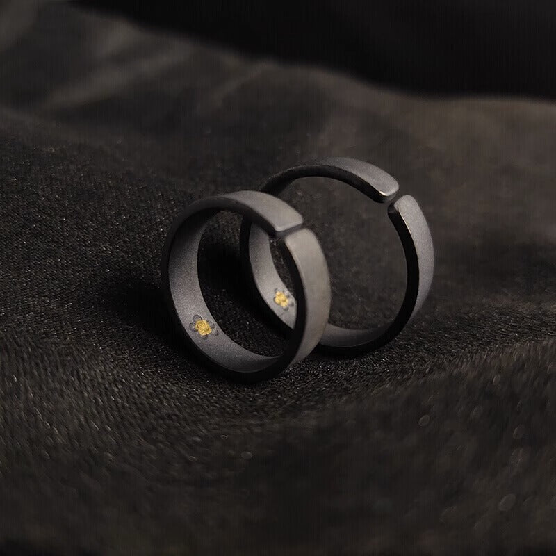 A pair of open-ended matte black rings with hidden gold details inside, resting on soft black fabric.