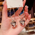 A woman with glossy manicure holding Silver 925 jewelry card displaying large silver hoop earrings with heart pendants