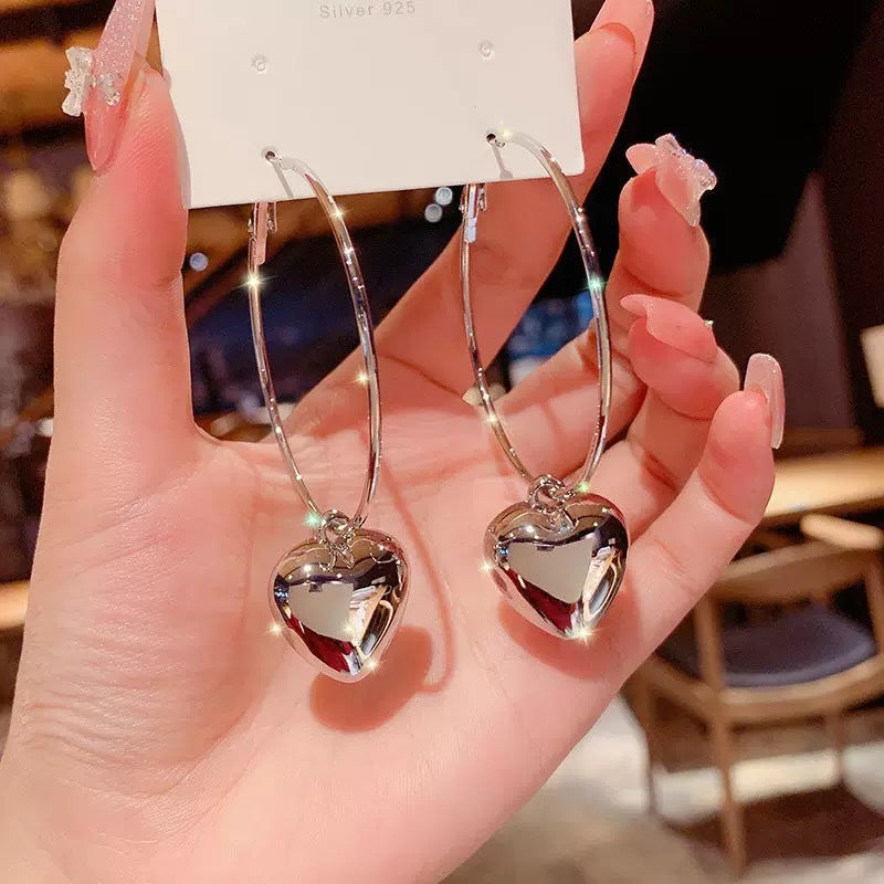 A woman with glossy manicure holding Silver 925 jewelry card displaying large silver hoop earrings with heart pendants
