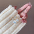 A woman's hand wearing cream sweater sleeve displaying elegant pearl drop earrings with crystal stud tops against neutral background