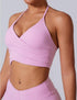 Woman wearing pink wrap-style workout crop top with ruched sides and matching leggings, showing navel piercing detail