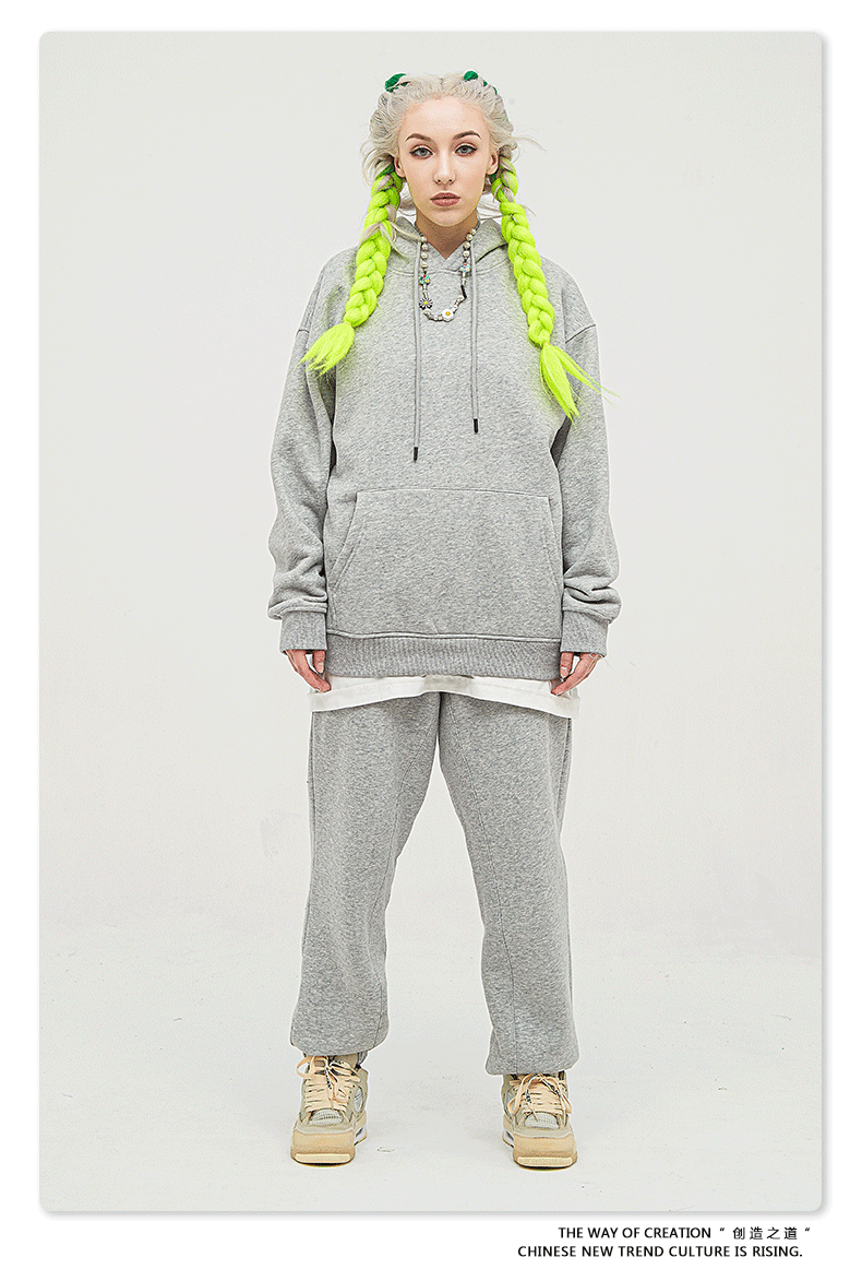 Model with platinum hair and neon yellow braids wearing an oversized gray sweatsuit featuring hoodie and matching joggers