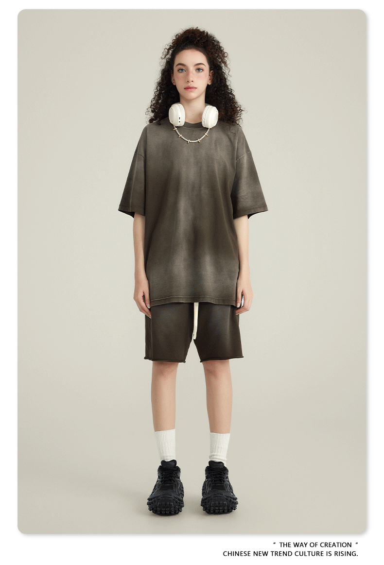 Model with curly hair wearing olive green t-shirt and matching shorts, with white headphones around neck, against cream background