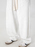 A close-up of wide-leg heather gray sweatpants with drawstring waist and curved seam details, paired with white athletic shoes