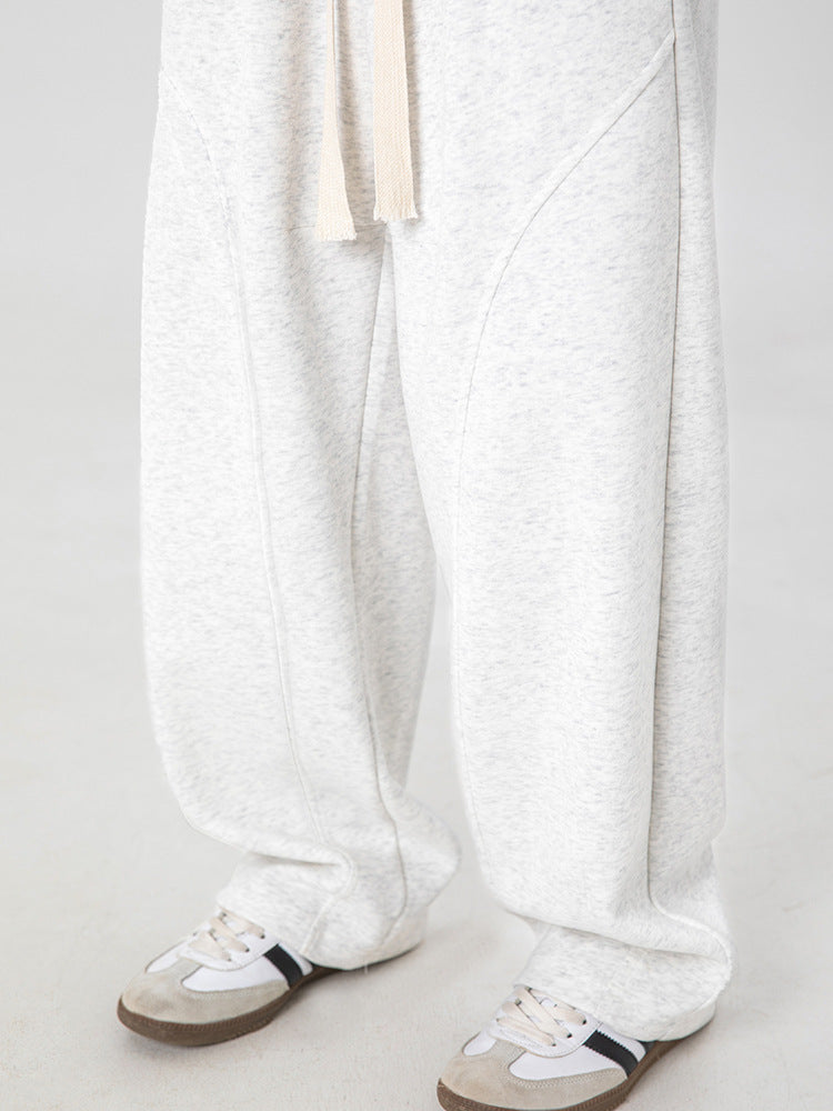 A close-up of wide-leg heather gray sweatpants with drawstring waist and curved seam details, paired with white athletic shoes
