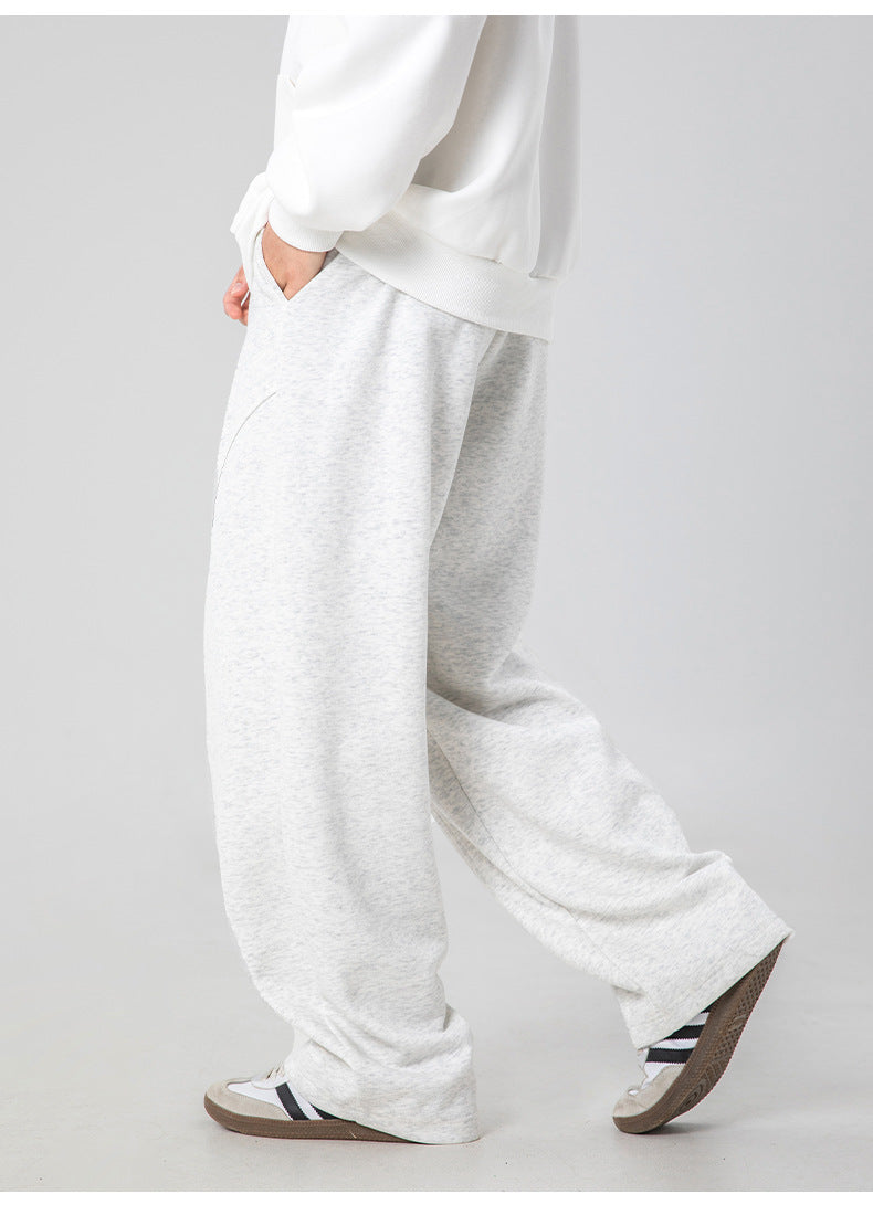 A model wearing white sweatshirt and relaxed-fit heather gray sweatpants, standing in profile view against neutral gray backdrop