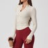 A woman wearing a cream ribbed long-sleeve top with v-neck collar and side ruching, paired with burgundy leggings, holding coffee cup against light background