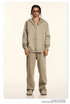 Model wearing beige oversized zip-up hoodie and matching sweatpants with gold-framed sunglasses and layered silver chain necklaces against cream background