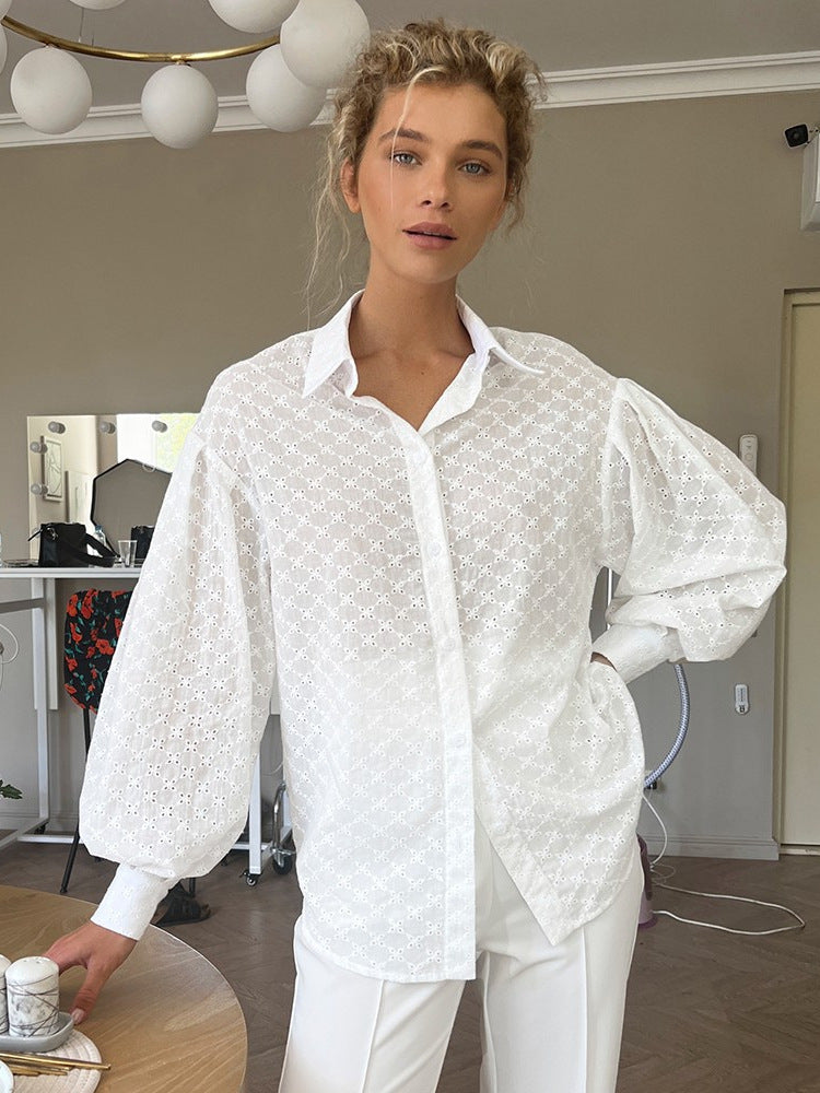 A woman wearing a white eyelet button-down shirt with voluminous balloon sleeves posing in an indoor setting with globe lights overhead