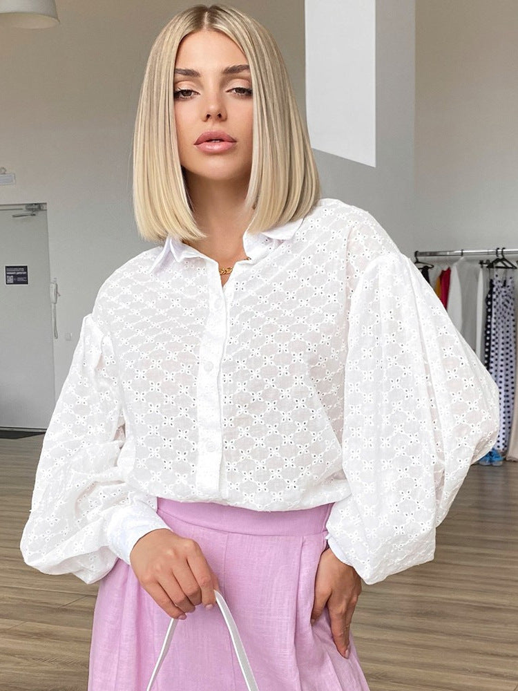 A woman with blonde bob haircut wearing a white eyelet button-down shirt with dramatic puff sleeves paired with lilac pants in a dressing room