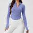 A model is wearing a periwinkle blue mandarin collar crop top with long sleeves and thumb holes paired with white leggings. Slim-fitting silhouette