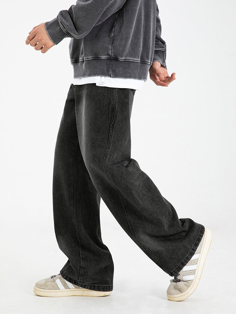 A model walking in black wide-leg denim jeans with visible seams, gray sweatshirt over white tee, paired with retro white and gray sneakers against white background