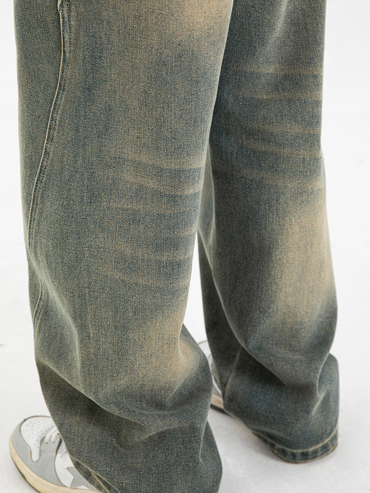 Close-up of olive-green wide-leg jeans showing faded wash pattern, distinctive vertical seams, and relaxed fit with gray sneakers visible at bottom