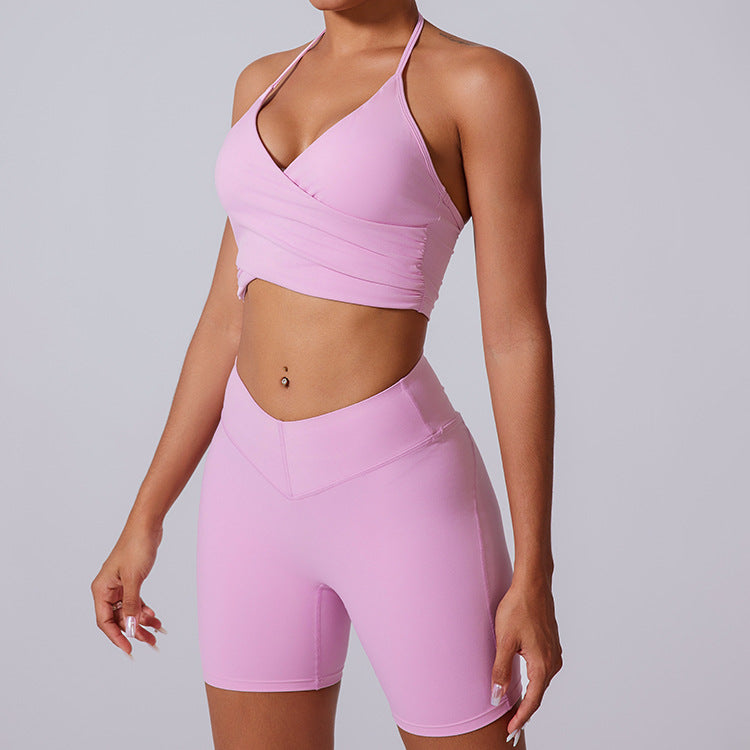 Pink workout set with halter neck sports bra and high-waisted biker shorts, featuring belly button piercing detail