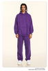 Model in purple hoodie and sweatpants set with white sneakers against cream backdrop