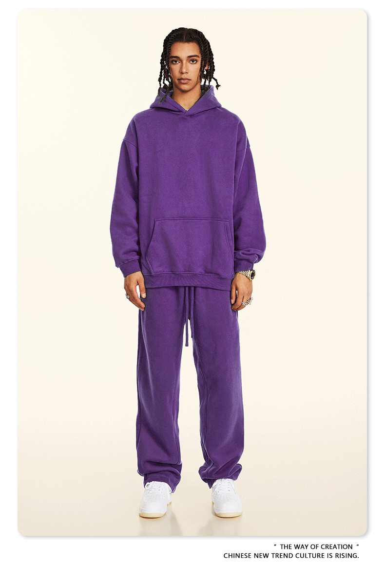 Model in purple hoodie and sweatpants set with white sneakers against cream backdrop