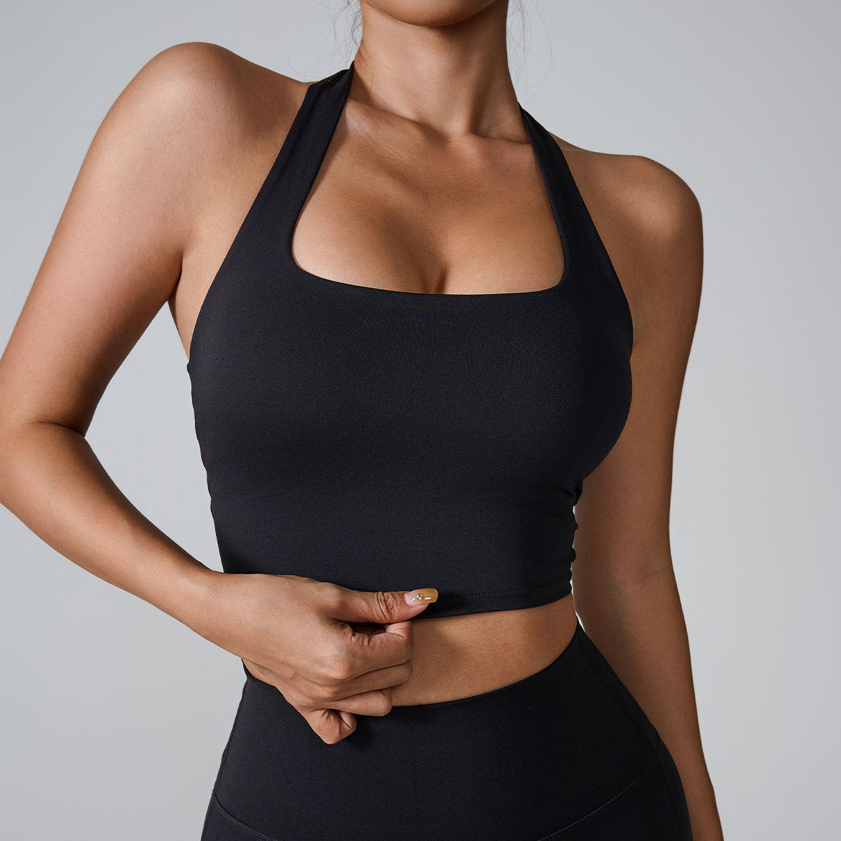 Model wearing black halter-style sports bra with square neckline and matching high-waist leggings against light gray background