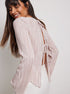 Back view of model smiling, showing open-back design with tie closures on pink pleated blouse
